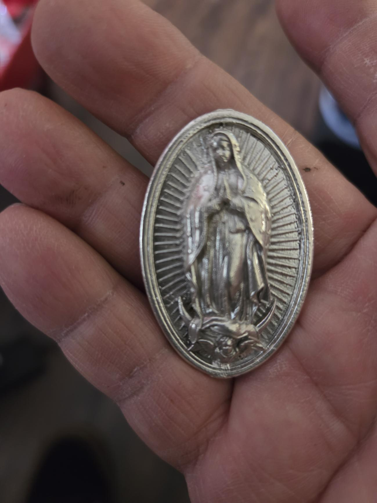 A silver Guadalupe medal in an open palm